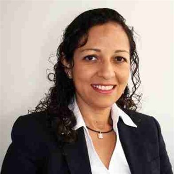Smiling woman with curly hair wearing a black blazer and white shirt.