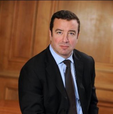 Man in a suit sitting, looking at the camera.
