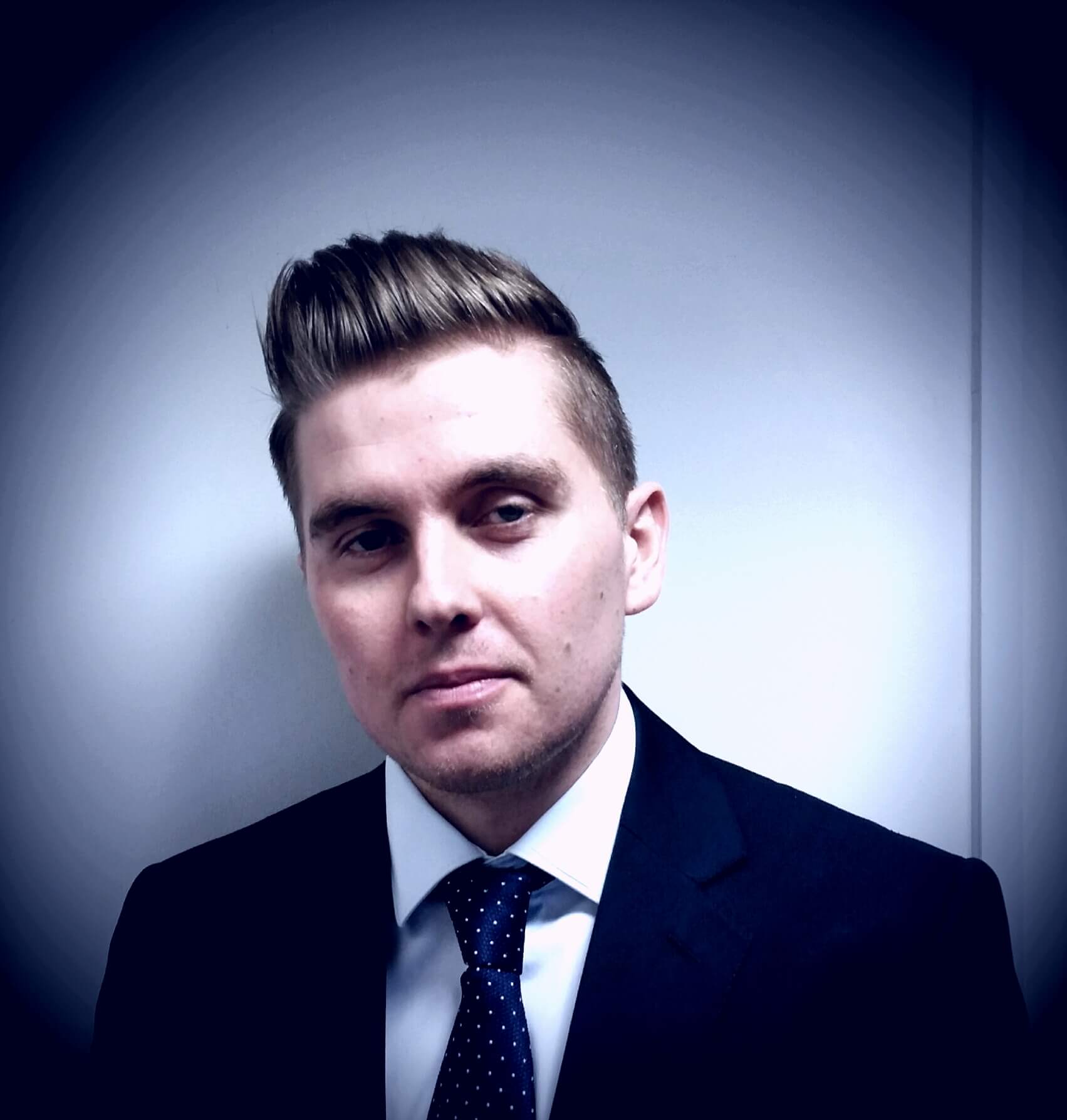 Man with short hair in a suit and tie against a white background.
