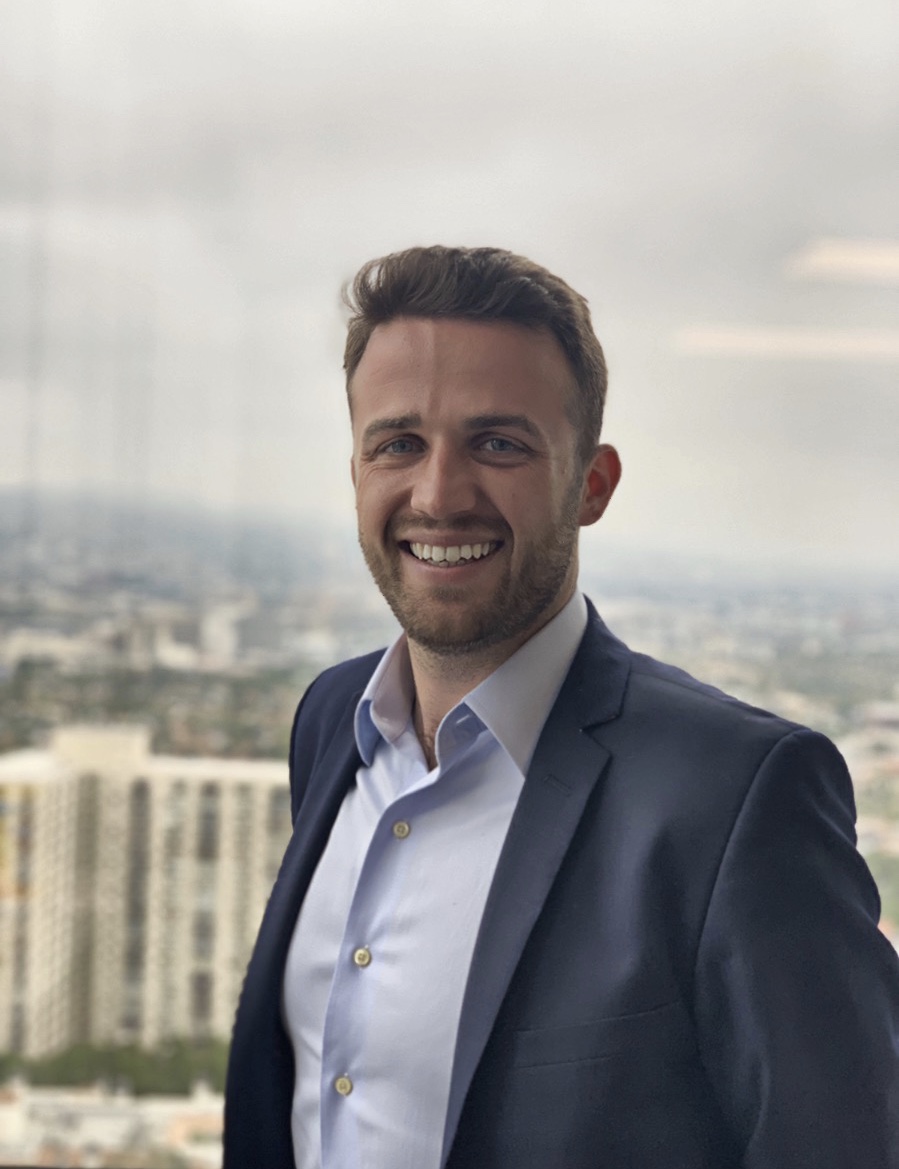 Smiling man in suit with cityscape in the background.