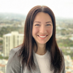 Smiling woman with long brown hair in a grey blazer, cityscape in background.