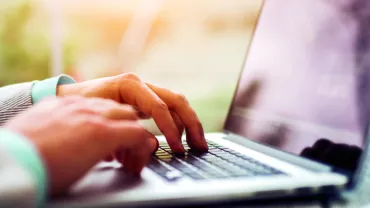 Person typing on a laptop at a desk, close-up view of the hands and keyboard.