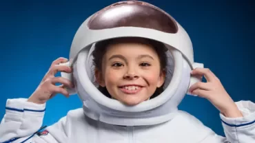 Smiling child wearing an astronaut helmet against a blue background.