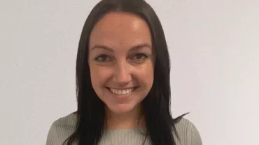 Smiling person with long dark hair against a plain background.