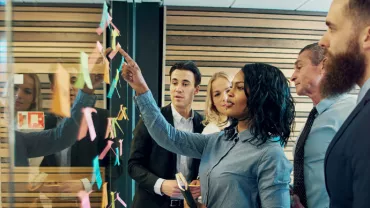 Business team collaborating with sticky notes on glass wall.