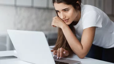 Woman in a white shirt using a laptop at a desk.