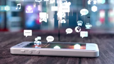 Smartphone with social media icons floating above its screen on a wooden table.