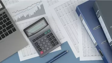 Laptop, calculator, and files on a desk with financial charts and documents.