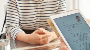 Person holding a tablet showing a resume during an interview at a glass table.