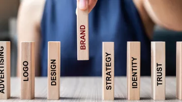 Hand holding a block with the word 'Brand' among other business-related blocks on a table.