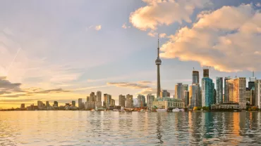 Panoramic view of a city skyline with a tall tower at sunset, reflecting on the water.