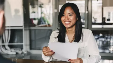 Smiling woman in a white blouse holding papers during a meeting.