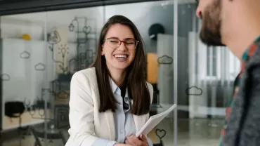 Smiling woman in glasses shaking hands in an office setting.