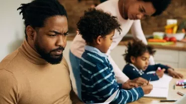 Family working together at a kitchen table with a laptop and books.