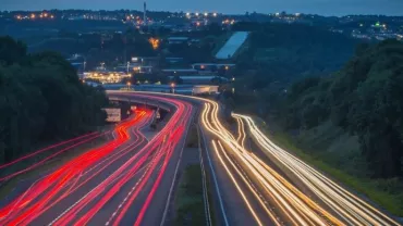 Night view of highway with light trails from vehicles under a dark, starless sky.