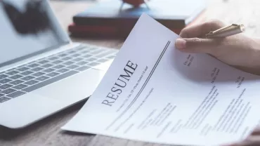 Person reviewing a resume near a laptop.
