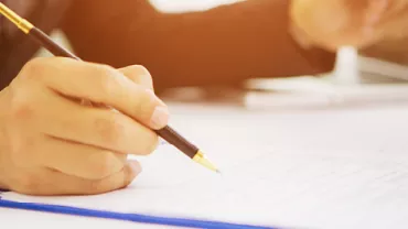 Person writing on a clipboard with a pen during a meeting.