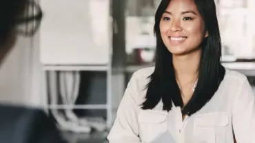 Woman smiling during a meeting, seated at a desk with documents.