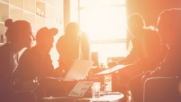 Group of people collaborating on laptops in a sunlit office.