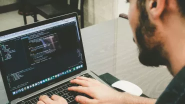 Person working on a laptop with code on the screen.