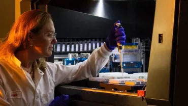 Scientist in lab coat using pipette in laboratory setting.