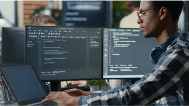 Person coding at a desk with multiple monitors displaying code.