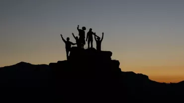 Group of people celebrating on a mountain peak at sunset.