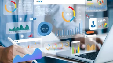 Person analyzing data visualizations on a laptop with graphs and charts displayed on a transparent screen.