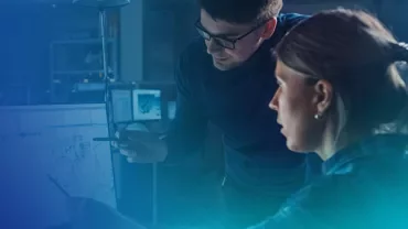 Two people discussing work at a computer screen in a dimly lit room.