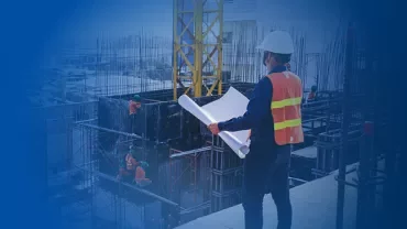 Construction worker reviewing blueprints on-site with crew and building framework.