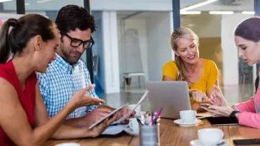 Group of colleagues having a discussion around a table with laptops and documents.