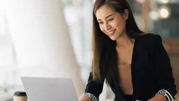 Woman smiling while using a laptop in a cafe.