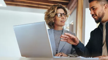 Two people discussing work at a desk with a laptop.