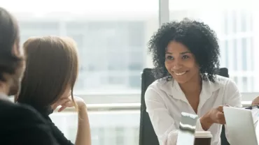 Woman smiling while holding papers in a meeting.