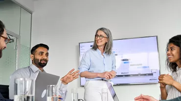 A diverse group of professionals in a meeting room discussing and smiling.