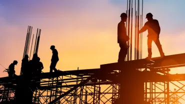Silhouette of construction workers on scaffolding at sunset.