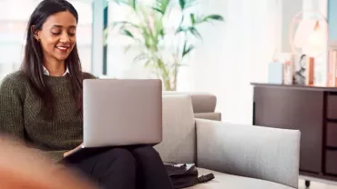 Woman sitting on a sofa using a laptop in a modern, bright office space.