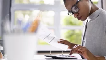 Woman calculating at desk with documents and monitor