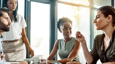 Four colleagues discussing at a meeting table in a bright office.