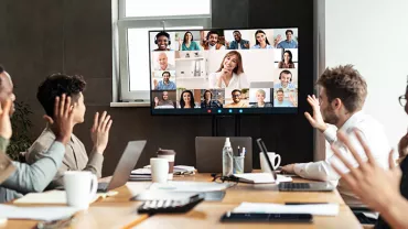 Team in a conference room participating in a video call with people displayed on a large screen.