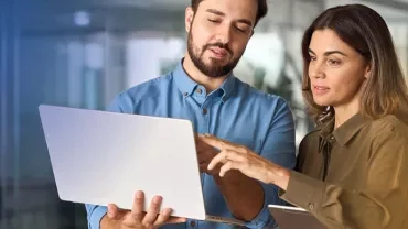 Two colleagues discussing work over a laptop in an office.
