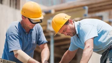 Two construction workers wearing hard hats working on a building site.