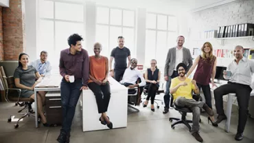 A diverse group of ten people in an office setting, smiling and posing together.