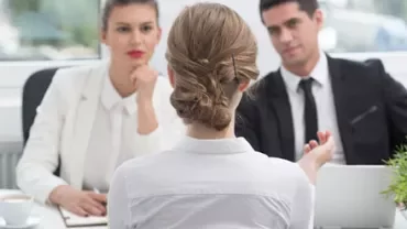 Person in a white shirt facing two interviewers across a table.