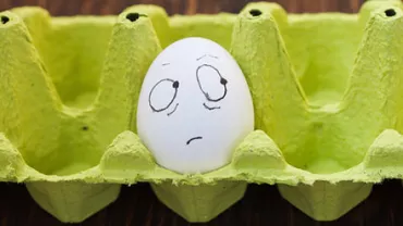 Egg with a drawn face showing confusion in a green egg carton.
