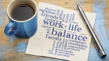 Coffee cup and pen on a table with a napkin featuring a word cloud about work-life balance.