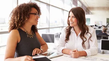 Two women smiling and talking in a bright office setting.