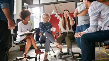 Group of colleagues laughing and chatting in an office setting.