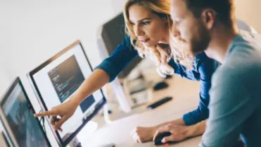Two people collaborating on computer screens displaying code.