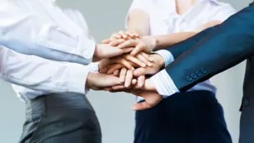 Group of people placing hands together in a teamwork gesture.
